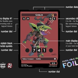 Op de afbeelding: Een rode kaart met een illustratie van een groene goblin met een paarse tong. De kaart heeft meerdere nummerweergaven en displays, waaronder een hoofddisplay en twee secundaire displays. De tekst bevat "GOBLIN" en "Token Creature - Goblin".