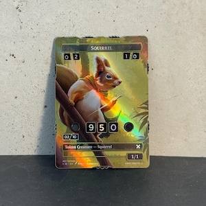 Puede incluir: Una tarjeta coleccionable holográfica con una ilustración de una ardilla. La tarjeta muestra la palabra "SQUIRREL" en la parte superior, junto con números y texto, incluyendo "Token Creature - Squirrel". La ardilla está representada en una rama, con una bufanda amarilla.