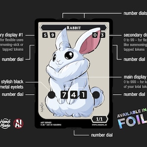 May include: A rectangular game token card featuring a white rabbit illustration. The card includes multiple number dials for tracking stats, labeled as secondary displays and a main display. Text includes Rabbit, 1/1, Art Series, and Available in Foil.