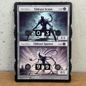 May include: A black and white card featuring two fantasy creatures, Eldrazi Scion and Eldrazi Spawn, with numerical values. The card has the text "TOKENX.ETSY.COM" and "EN 2026".