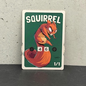 May include: A card featuring a cartoon squirrel with orange and brown fur, a white belly, and an angry expression. The word "SQUIRREL" is at the top, with the numbers "4" and "6" below the squirrel. The card is green and white.