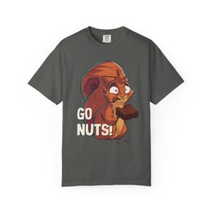 Puede incluir: Una camiseta gris carbón de manga corta con una ilustración gráfica de una ardilla marrón de ojos muy abiertos comiendo un brownie de chocolate. El texto GO NUTS! está impreso en letras mayúsculas blancas a la izquierda de la ardilla.