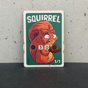 Könnte beinhalten: Rechteckige Karte mit einem Cartoon-Eichhörnchen mit orangefarbenem Fell und überraschtem Gesichtsausdruck. Das Wort "SQUIRREL" steht oben, mit den Zahlen "30" und "1/1" sichtbar. Der Hintergrund ist grün.