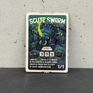 Pode incluir: Um cartão colecionável com o texto "SCUTE SWARM" e uma ilustração de um inseto. O cartão tem uma borda verde e mostra os números "999" e "1/1". O texto descreve as habilidades do cartão.