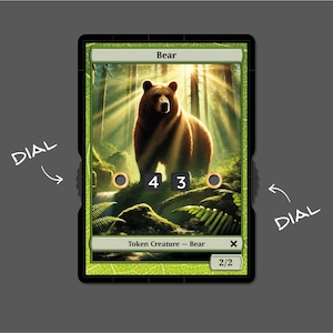 Könnte beinhalten: Eine braune Bären-Token-Kreaturenkarte mit grünem Hintergrund und dem Text "Bär" oben. Die Karte hat eine Stärke und Zähigkeit von 2/2. Die Karte ist Teil eines Spiels.