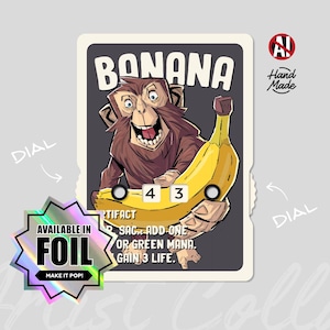 Puede incluir: Una tarjeta de juego rectangular que muestra un mono marrón sosteniendo un plátano amarillo grande. La tarjeta muestra el texto BANANA, incluye dos diales blancos que muestran los números 4 y 3, y tiene una pegatina holográfica en forma de estrella AVAILABLE IN FOIL.
