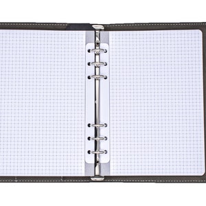 Może przedstawiać: Szary notes w skórzanej oprawie z piórem przymocowanym do okładki. Notes ma kratkę na stronach i metalowy segregator.
