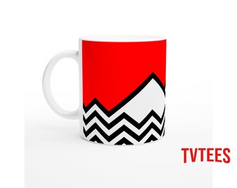 May include: White ceramic mug with a red top section, a white mountain-like design, and a black and white zigzag pattern. The text "TVTEES" is printed in red on the bottom right.