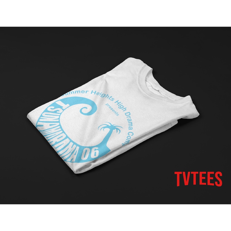 May include: White t-shirt with a light blue graphic design. The design includes the text "Tsunami Drama 06" in a curved font, along with "Summer Heights High Drama Company presents" and a stylized palm tree.