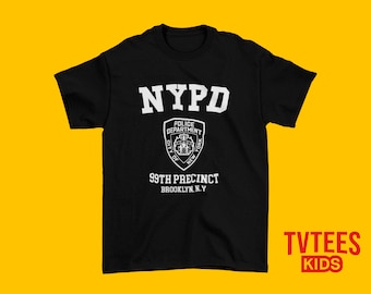May include: Black t-shirt with the white text "NYPD" at the top, and a police badge graphic below. The text "99th Precinct Brooklyn N.Y." is printed below the badge. The shirt has short sleeves.