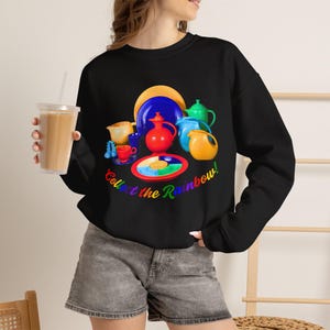 May include: A black long-sleeve sweatshirt featuring a colorful graphic of various ceramic kitchenware items in shades of red, blue, yellow, and green, with the text "Collect the Rainbow!" printed in a multi-colored arc underneath the dishes.