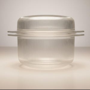 May include: Clear glass container with a lid. The container has vertical ribbed detailing and two horizontal handles. The lid is rounded and also has vertical ribbed detailing. The container is likely for food storage.