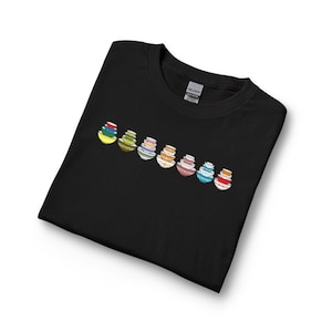 May include: Black t-shirt featuring a row of colorful, stacked bowls. Each bowl stack has a unique design and color scheme, including yellow, green, orange, pink, and blue. The shirt is made of a soft material.