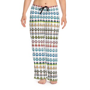 May include: White pajama pants with a repeating pattern of colorful, stacked, cartoon-style pots. The pots are in various colors, including red, blue, yellow, and green. The pants have a black drawstring.