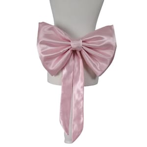 May include: A large pink satin bow with long tails. The bow is tied around a white chair sash.