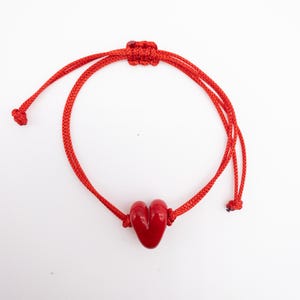 Pode incluir: Pulseira de corda vermelha com um charme de coração vermelho.