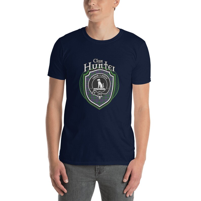 May include: A navy blue t-shirt with a white graphic of a clan crest. The crest features a white dog, a green and purple tartan, and the text "Clan Hunter" in a white circle.