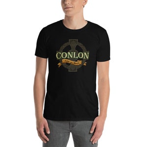 May include: Black t-shirt featuring a Celtic cross design with the name "CONLON" in a green and gold font. The shirt includes the text "Erin go Bragh" on a gold banner. The design is centered on the chest.