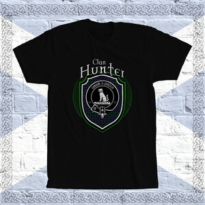 May include: Black t-shirt with a green and purple clan crest featuring a white dog and the text "Clan Hunter" and "Cunsum o perfido".