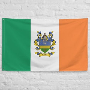 May include: An Irish flag with a coat of arms featuring a shield with a blue and white eagle, a green and yellow shield, and a green and gold shield. The coat of arms is surrounded by gold and green floral designs. The text "Conlon" is written on a blue ribbon below the shield.