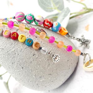 May include: A colourful beaded keychain with the word "breathe" spelled out in gold letters. The keychain also features a small silver charm with a heart design.