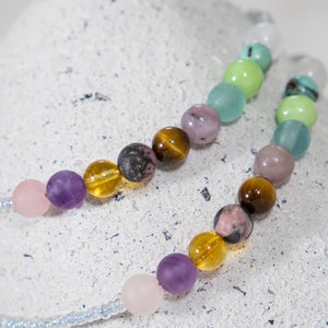 May include: A multi-colored beaded necklace with a variety of gemstone beads, including amethyst, rose quartz, tiger's eye, and green aventurine.