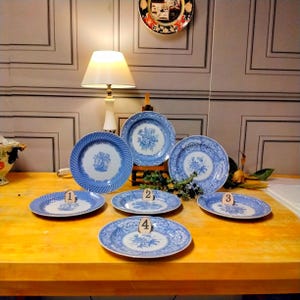 May include: Six blue and white porcelain plates with floral designs. The plates are arranged in a circle on a wooden table. The plates are numbered 1 through 4.