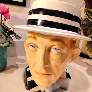 May include: A ceramic planter shaped like a person's head wearing a white and black striped hat. The planter has a white and black striped collar.