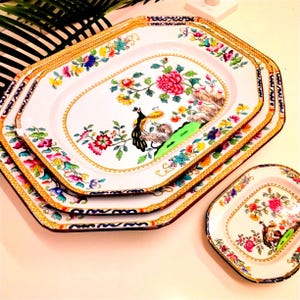 May include: A set of four decorative serving platters with a white background and a colorful floral and bird design. The platters have gold trim and an octagonal shape. The largest platter measures approximately 40 cm long.