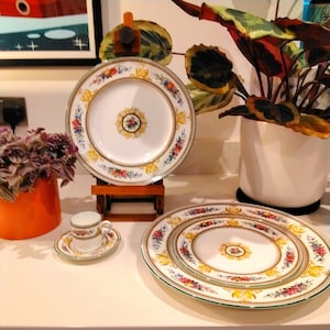 May include: A set of three white porcelain plates with a floral design in shades of pink, yellow, and green. The plates are nested together, with the smallest plate in the center and the largest plate on the outside. The plates have a gold trim around the edges.