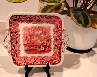 May include: A square, red and white ceramic serving tray with a floral design and two handles. The tray features a central scene of a building and trees in a landscape.