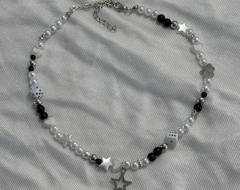 May include: A white pearl necklace with black beads, silver charms, and a large silver star pendant. The charms include dice, hearts, and stars.