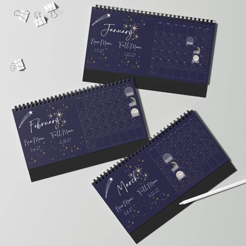 May include: Three spiral-bound desk calendars featuring a dark blue background with gold celestial illustrations of stars, shooting stars, and moon phases. Each page displays the month name, New Moon and Full Moon dates, and a grid of days.