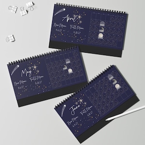 May include: Three spiral-bound desk calendars for April, May, and June 2027, featuring a dark blue background with gold stars, a shooting star, and moon phase illustrations. Each page displays the month name, New Moon and Full Moon dates.