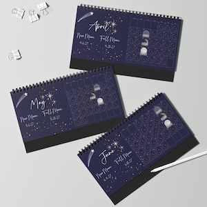 May include: Three spiral-bound desk calendars for April, May, and June 2027, featuring a dark blue background with white celestial illustrations of stars, shooting stars, and moon phases. Each page displays a monthly grid with lunar cycle dates.