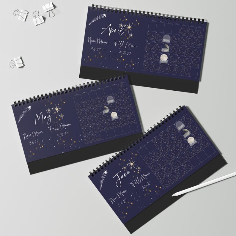 May include: Three spiral-bound desk calendars for April, May, and June 2027, featuring a dark blue background with white celestial illustrations of stars, shooting stars, and moon phases. Each page displays a monthly grid with lunar cycle dates.