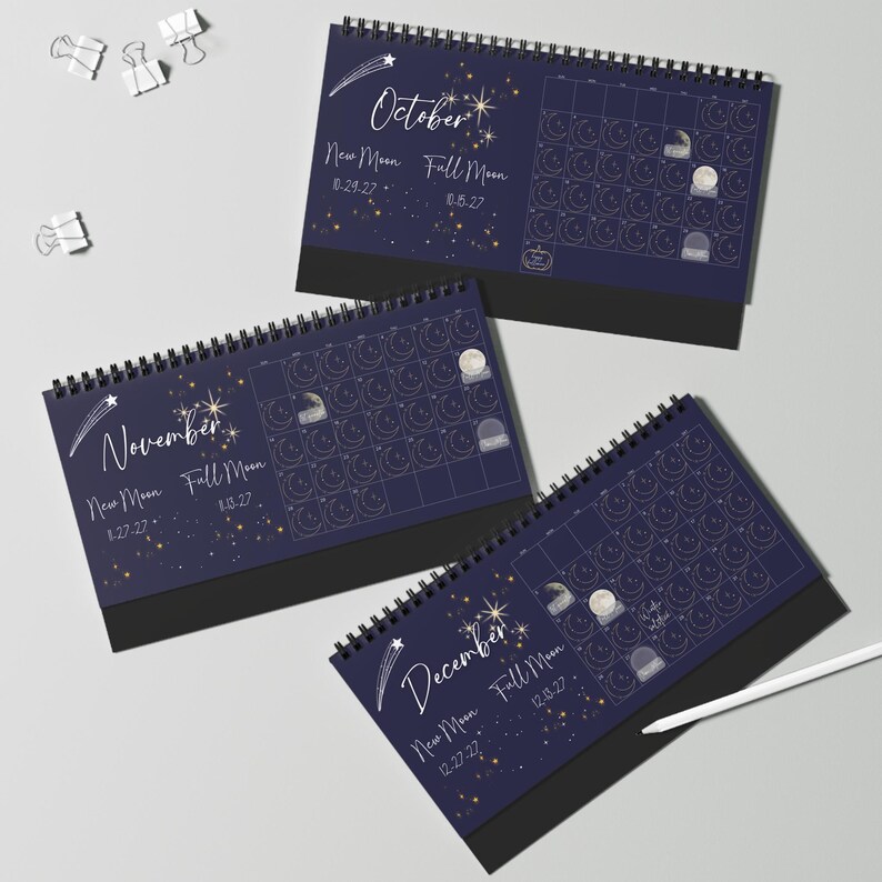 May include: Three spiral-bound desk calendars for October, November, and December 2027. Each dark blue page features celestial graphics, moon phase dates, and a grid layout. The calendars include text for New Moon and Full Moon dates.