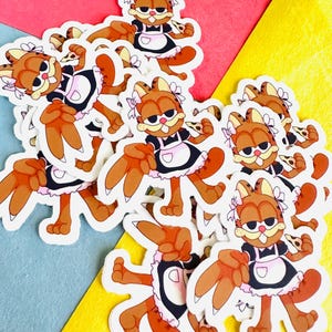 May include: A pile of stickers featuring a cartoon cat dressed as a maid holding a slice of pizza. The cat has orange fur, a pink bow, and a black and white maid outfit. The stickers are on a colorful background.