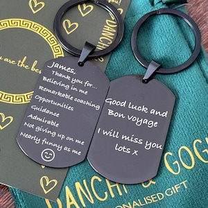 May include: Two black metal keychains with engraved messages. The keychain on the left says "James, Thank you for... Believing in me Remarkable coaching Opportunities Guidance Admirable Not giving up on me Nearly funny as me". The keychain on the right says "Good luck and Bon voyage I will miss you lots x".