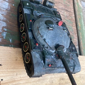 May include: A green toy tank with a rusty barrel and a gray turret. The tank has a red circle on the turret and a yellow stripe around the wheels.