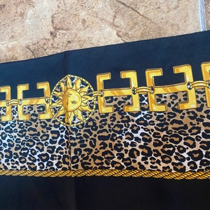 May include: Black fabric with a gold chain pattern and a gold sun with a face in the centre. The chain pattern is on top of a brown and black leopard print.