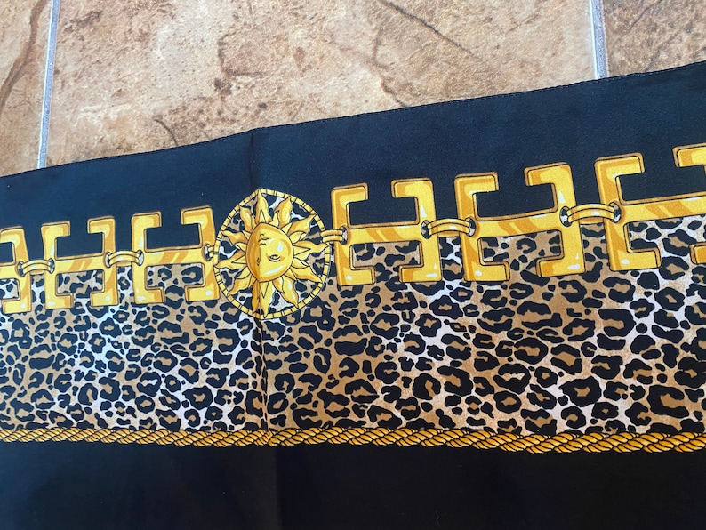 May include: Black fabric with a gold chain pattern and a gold sun with a face in the centre. The chain pattern is on top of a brown and black leopard print.
