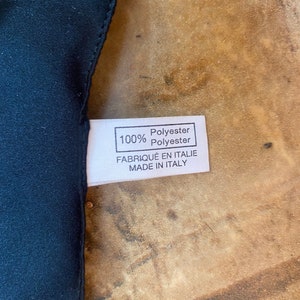May include: A white fabric label with black text that reads "100% Polyester Polyester Fabriqu&eacute; en Italie Made in Italy".