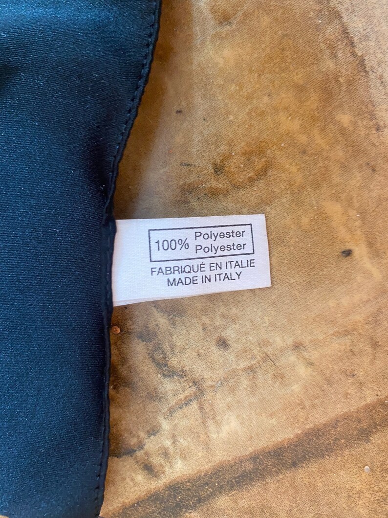 May include: A white fabric label with black text that reads "100% Polyester Polyester Fabriqu&eacute; en Italie Made in Italy".