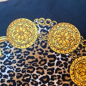 May include: A black fabric with a leopard print pattern and gold chain with circular medallions. The medallions have a floral design.