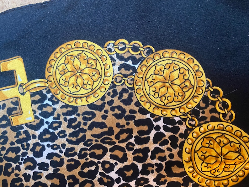 May include: A black fabric with a leopard print pattern and gold chain with circular medallions. The medallions have a floral design.