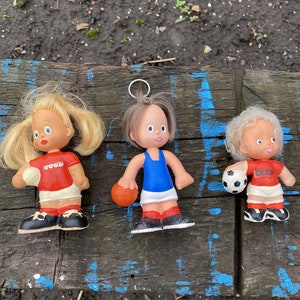 Op de afbeelding: Drie kleine plastic poppen die sportuniformen dragen met het woord "CCCP" op hun shirts. De poppen houden ballen vast en staan op een houten oppervlak.