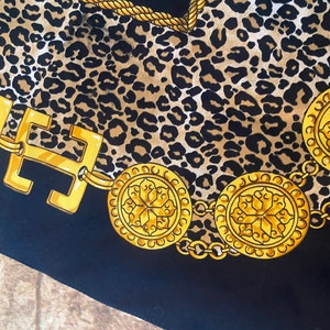 May include: A black fabric with a leopard print pattern and a gold chain with decorative medallions. The chain is made of interlocking links and the medallions have a floral design.