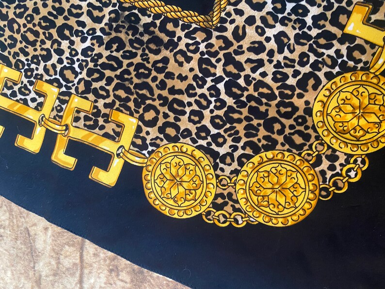 May include: A black fabric with a leopard print pattern and a gold chain with decorative medallions. The chain is made of interlocking links and the medallions have a floral design.