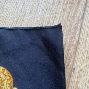 May include: A black silk scarf with a gold and yellow chain pattern. The scarf has a finished edge.
